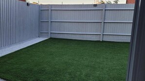 Patio trasero con cerramiento, césped sintético y una pequeña zona de grava.