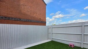 Un patio trasero cercado con césped artificial y un edificio de ladrillo.