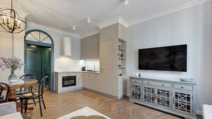 Een moderne keuken met witte kasten, een eethoek met een houten tafel en stoelen, en een grote flatscreen televisie aan de muur.