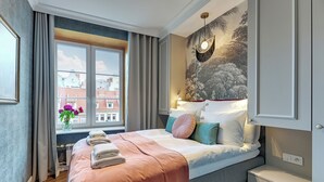 Een moderne slaapkamer met een groot bed, een nachtkastje, een wandlamp en een raam met gordijnen.