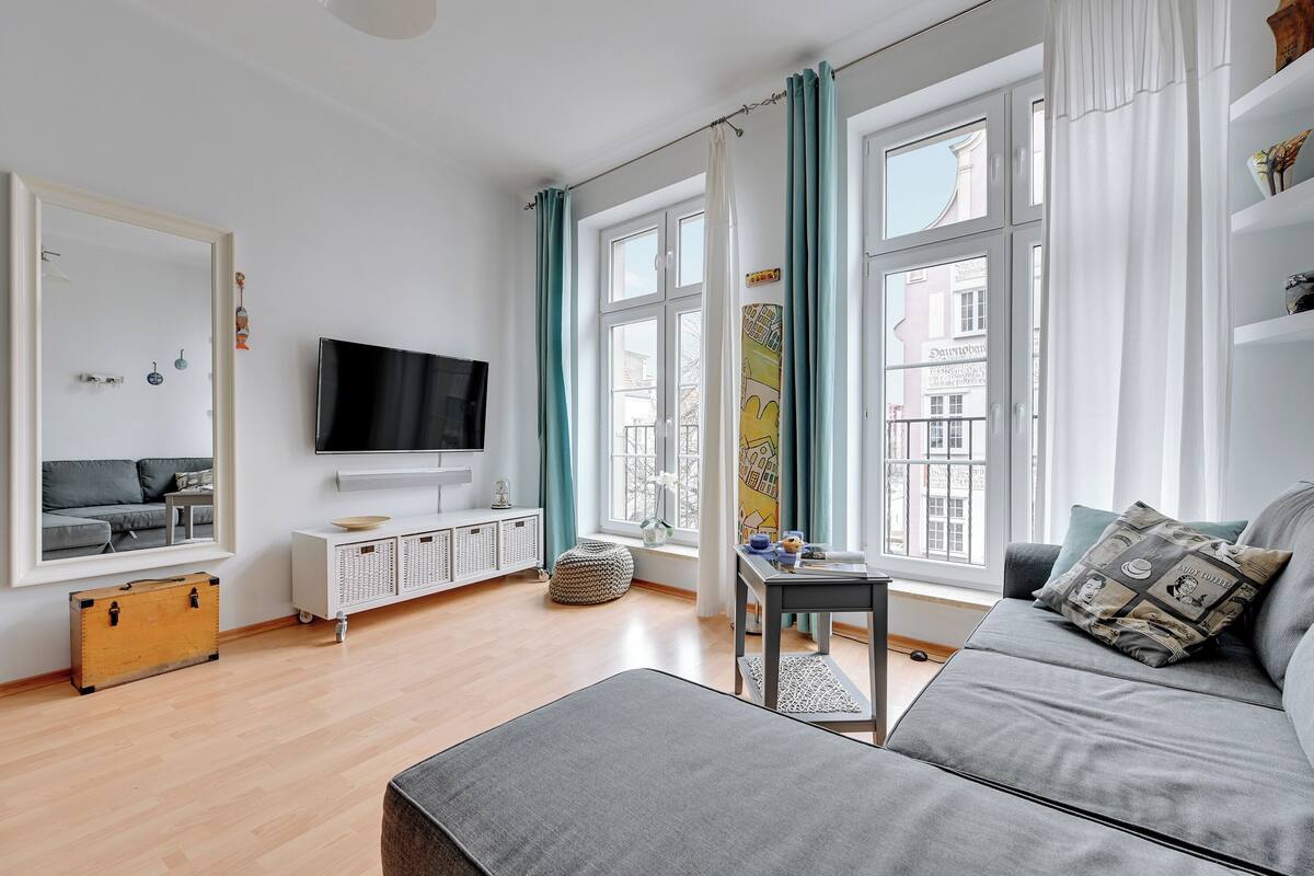 A modern living room with a sofa, a TV, a small table, and a window with curtains.