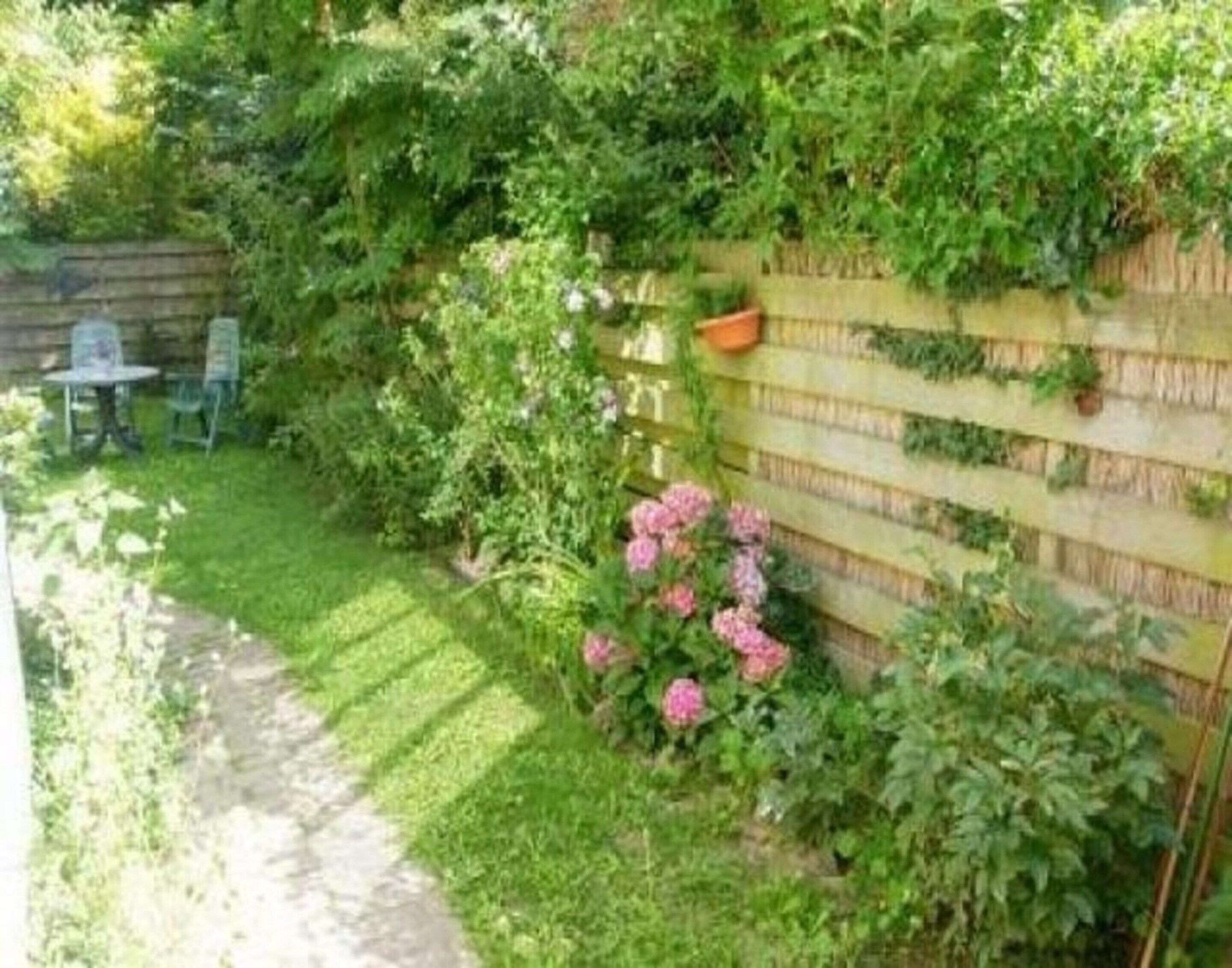 Een tuin met een houten omheining, een tafeltje en stoelen.