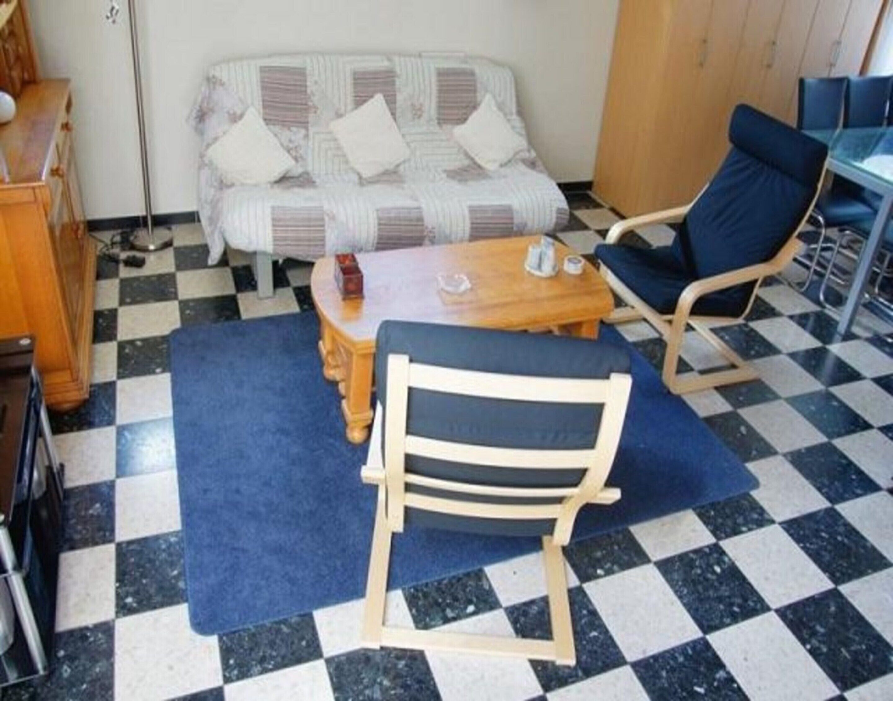 A room with a checkered floor, a sofa with patterned cushions, a wooden coffee table, and a blue chair.