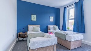 Ein Schlafzimmer mit zwei Betten, einem Nachttisch und einem Fenster mit blauen Vorhängen.