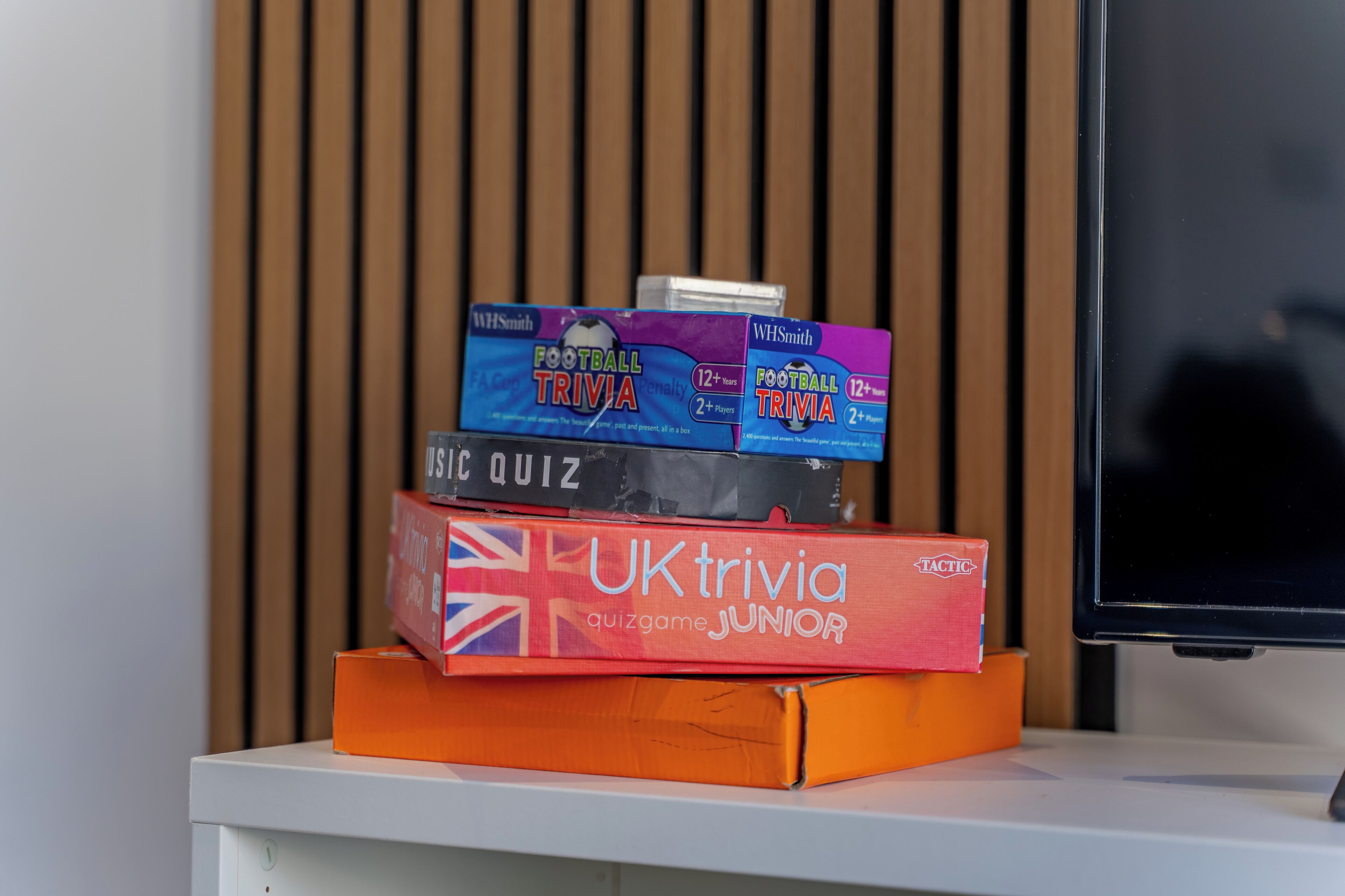 Une pile de boîtes de jeux de questions-réponses sur une surface blanche, avec un téléviseur en arrière-plan.