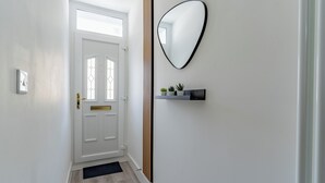 Ein Flur mit einer weißen Tür, einem Spiegel mit schwarzem Rahmen und einem kleinen Regal mit Pflanzen.