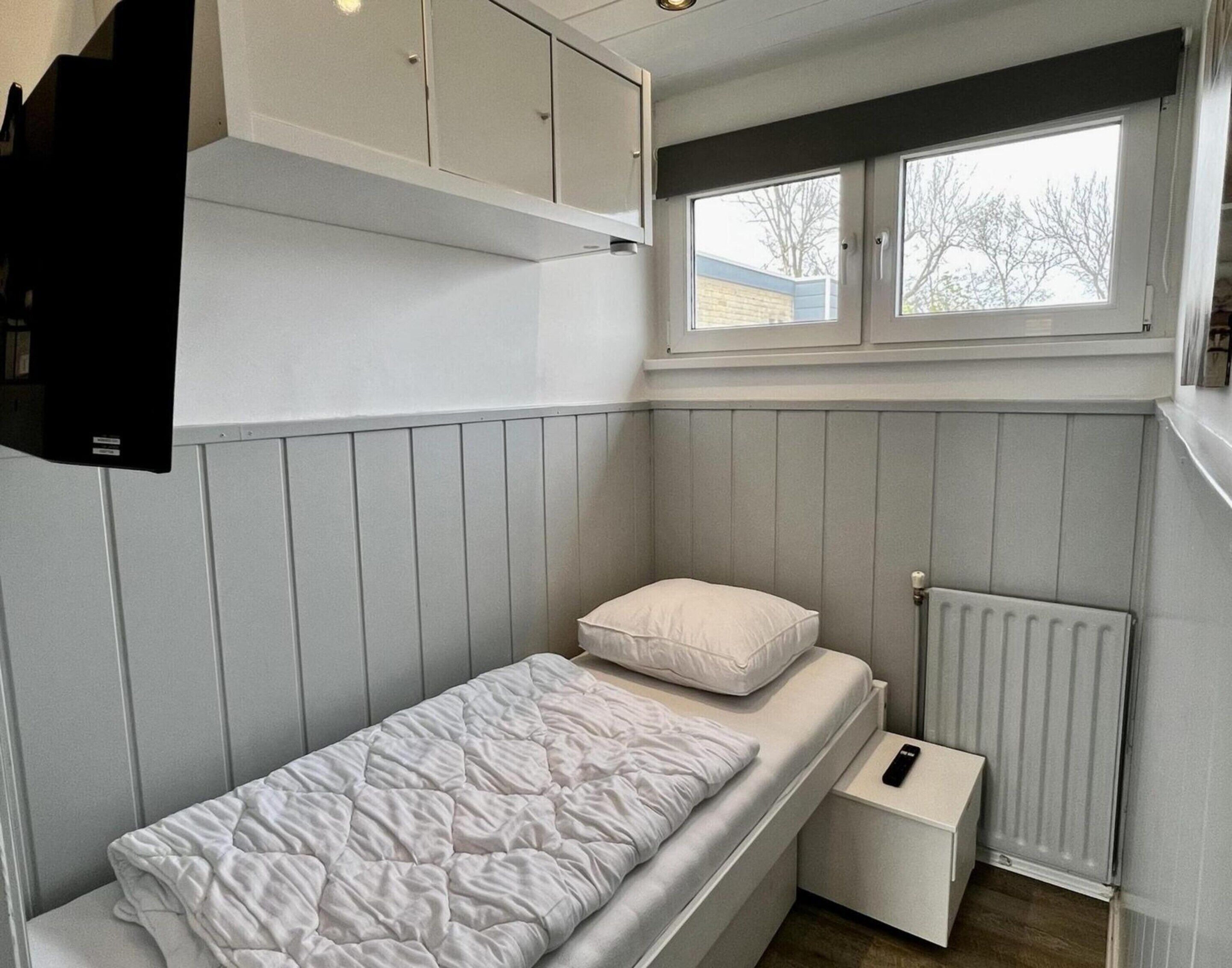 A small, compact bedroom with a bunk bed, a window, a radiator, and a white wardrobe.