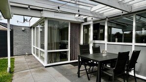 A covered patio with a table and chairs, large windows, and a view of the surrounding area. - Beautiful Bungalow in North Holland (Sint Maartensvlotbrug)