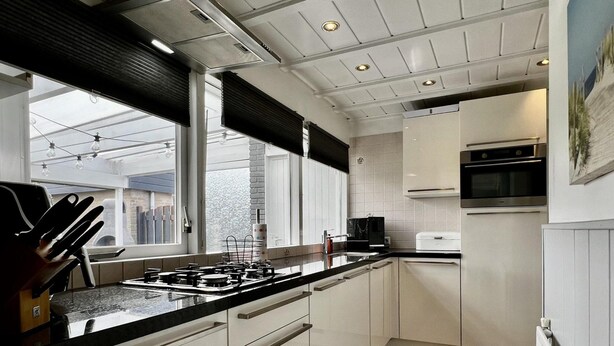 A modern kitchen with a gas stove, white cabinets, and a black countertop. - Beautiful Bungalow in North Holland (Sint Maartensvlotbrug)