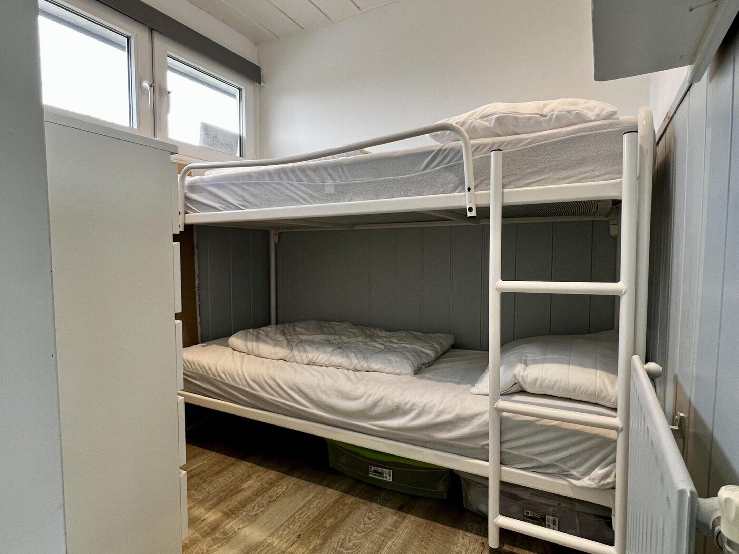 A bunk bed room with a window, a radiator, and a wooden floor.