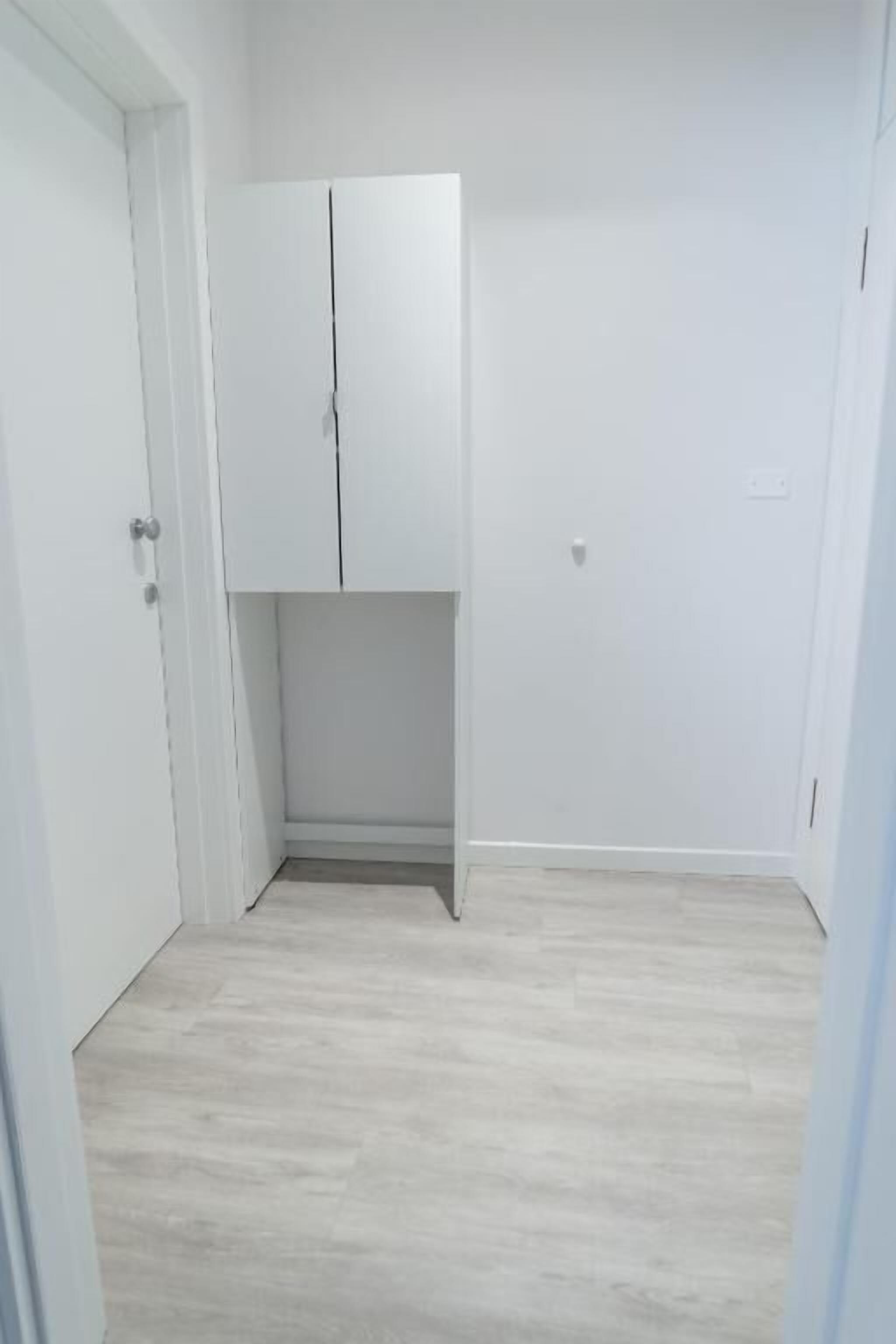 A room with a white wardrobe, a door, and a light-colored wooden floor.