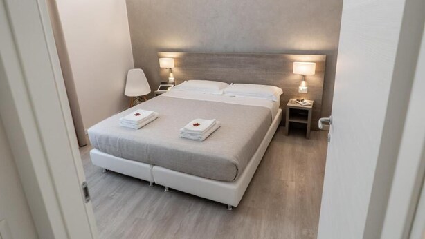 A modern hotel room with a large bed, two bedside tables, and wall-mounted lamps. - DOLCE NOTTE APARTMENTS (Verona)