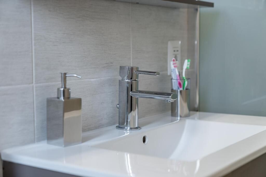 Une salle de bain moderne avec un lavabo blanc, deux robinets chromés et un porte-brosse à dents contenant une brosse à dents.