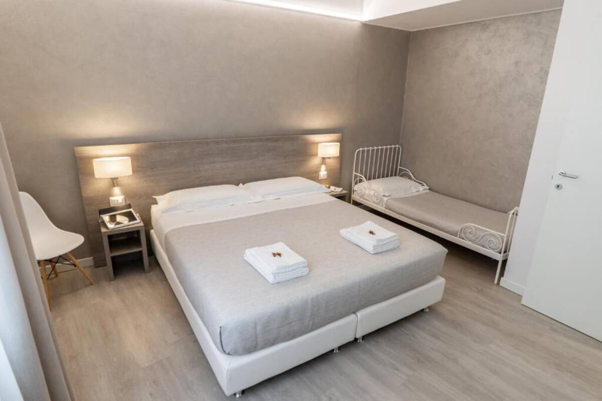 Una habitación de hotel moderna con una cama grande, una cama más pequeña, una silla y una mesita de noche con una lámpara.