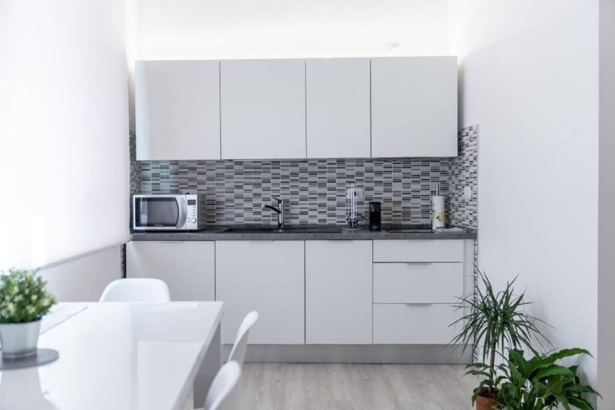 Una cocina moderna con armarios blancos, microondas, cafetera y salpicadero de azulejos.