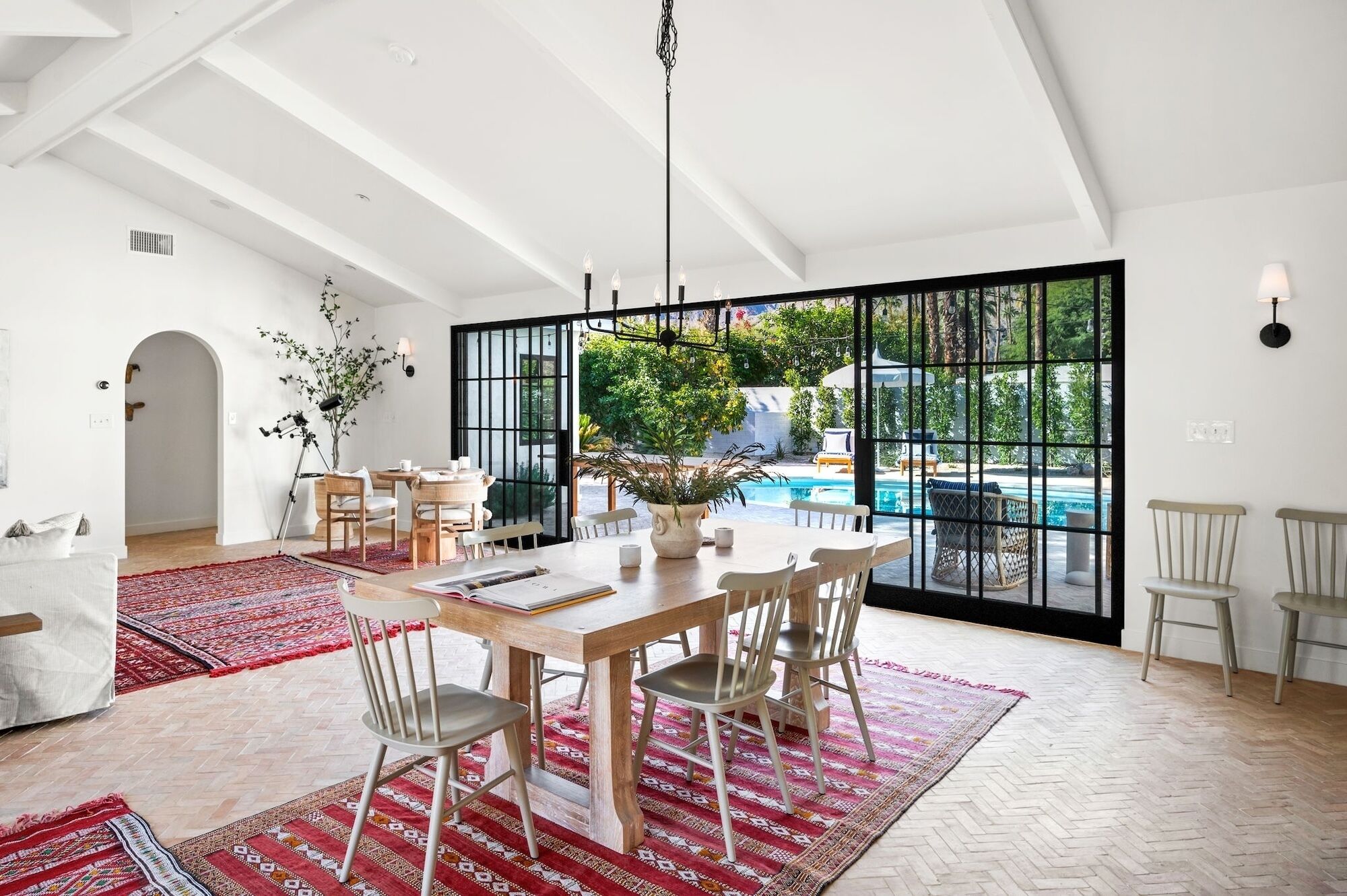 Un vaste espace dédié à la salle à manger, avec une grande table et des chaises, une vue sur une piscine et une grande fenêtre aux montants noirs.