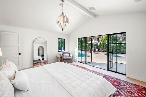 A bedroom with a large bed, a mirror, and a view of an outdoor swimming pool through a sliding glass door.