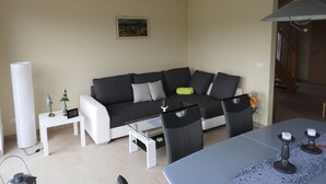 Ein modernes Wohnzimmer mit einem grauen Sofa, einem weißen Couchtisch und schwarzen Stühlen. An der Wand hängt ein Bild, eine Lampe und ein kleiner Tisch mit Dekoration.