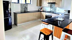 Una cocina moderna con una isla central, estufa y lavaplatos. Hay dos taburetes y un refrigerador.