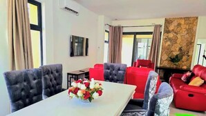 Una sala de estar moderna con una mesa de centro blanca, sillas tapizadas en rojo y gris, una chimenea y una pared de acento de piedra.