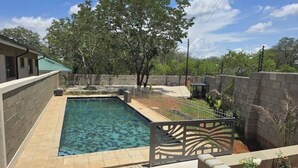 Una piscina con plataforma de baldosas, rodeada por un muro de piedra y una valla de metal.