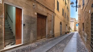 A narrow cobblestone street flanked by buildings with stone walls and wooden doors. - Sardinia Re - Maiorca 13 (Alghero)