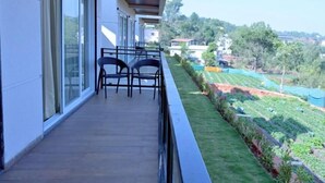 A balcony with a table and chairs, overlooking a green landscape with buildings in the distance.