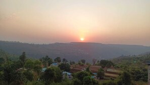 A rural landscape with a sunrise or sunset, houses, and a hilly terrain. - Mountain Berries Resort (Mahabaleshwar)