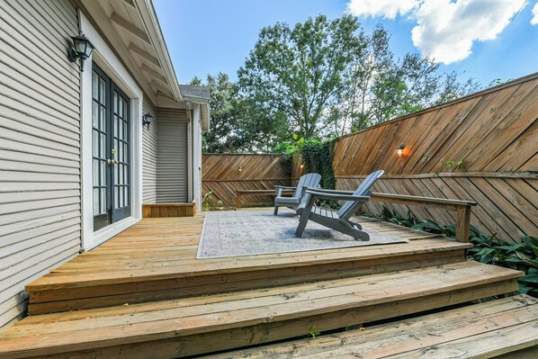 A wooden deck with steps leading to a covered patio area, two lounge chairs, and a wooden fence with climbing plants. - Beverly is a charming 1925 cottage-style bungalow in The Heights, sleeping 4 (2B/1B) and filled with natural light. Walk to the jog track, tennis courts, and local shops/eateries. Enjoy a fenced, pet-friendly yard, front porch swing, and back patio. (Houston)