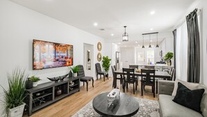 Una sala de estar moderna con un televisor de pantalla plana, muebles de madera oscura y un comedor con una cocina al fondo.