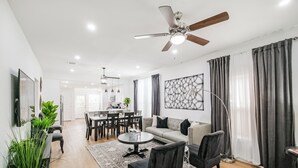 Una sala de estar moderna con un sofá, sillones, una mesa de centro, un televisor y un ventilador de techo.