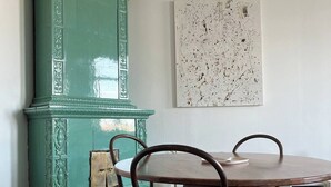 Een eetgedeelte met een ronde houten tafel en vier stoelen, een blauwgroene kast en een groot abstract schilderij aan de muur.