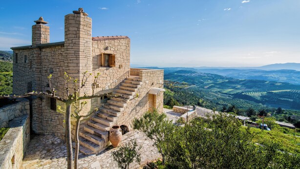 A stone building with a staircase leading to a wooden door, surrounded by lush greenery and a panoramic view of the countryside. - Panoramic View Villa in OliveGroves (Loutraki)