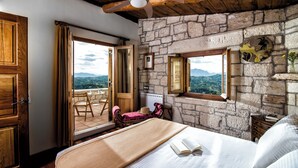 A bedroom with a stone wall, wooden ceiling, and a bed with an open book. - Panoramic View Villa in OliveGroves (Loutraki)