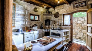 A rustic kitchen with stone walls, wooden beams, and a wooden table with bread and cheese. - Panoramic View Villa in OliveGroves (Loutraki)
