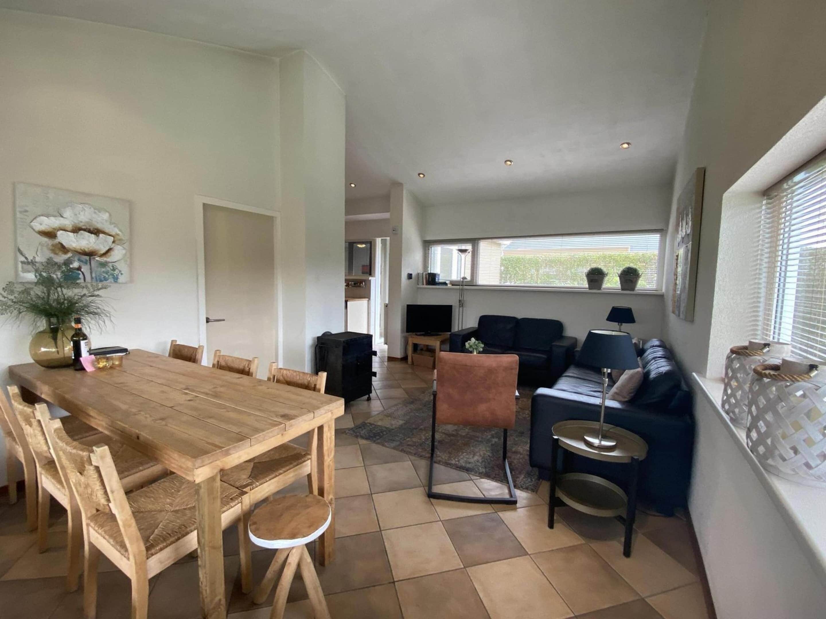 A spacious living area with a wooden dining table, a sofa, and a TV.
