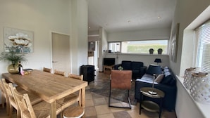 A spacious living area with a wooden dining table, a sofa, and a TV. - Lovely Holiday Bungalow With Garden (Sint Maartensvlotbrug)