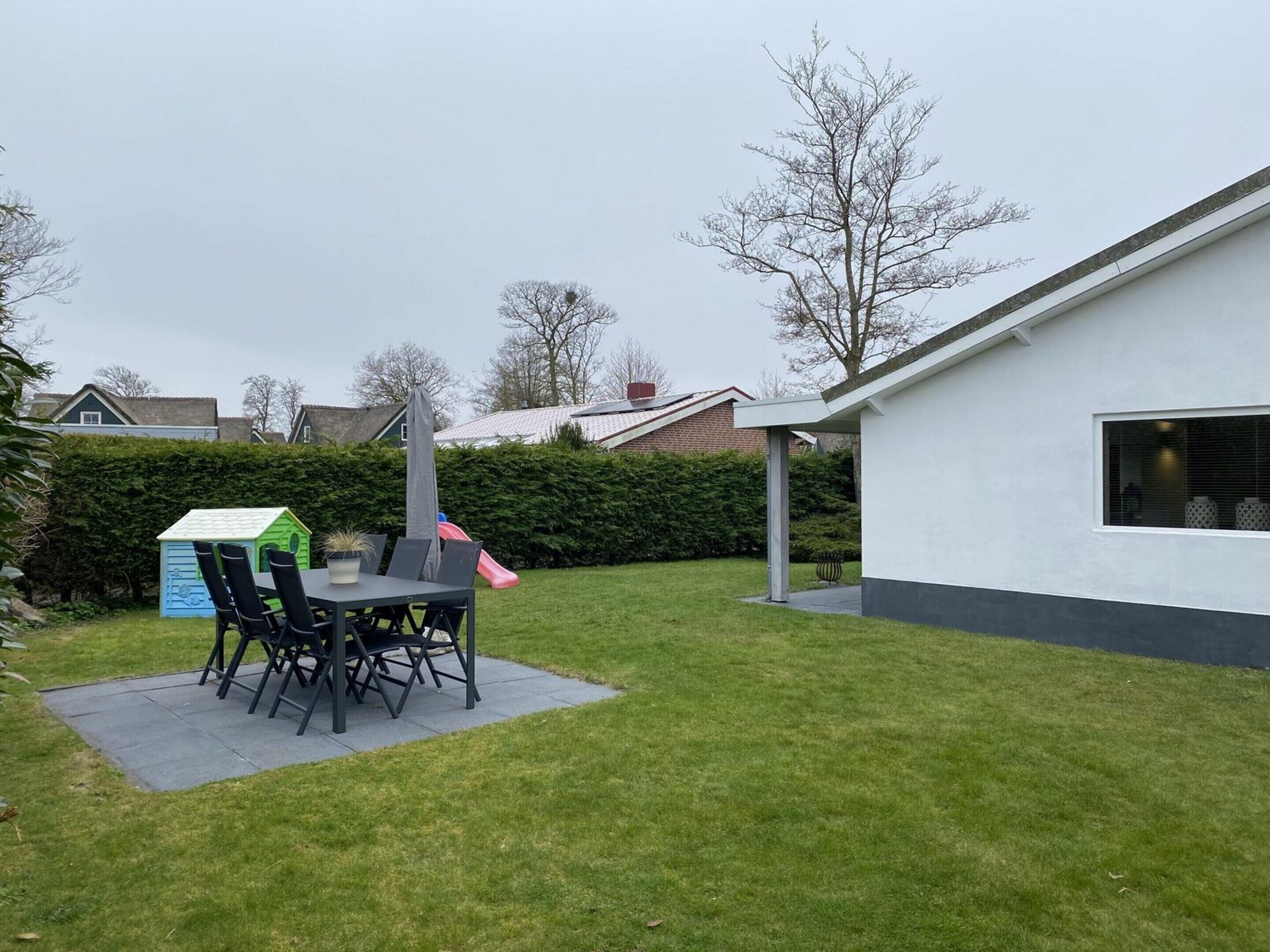 A backyard with a dining table and chairs, a playhouse, and a slide.