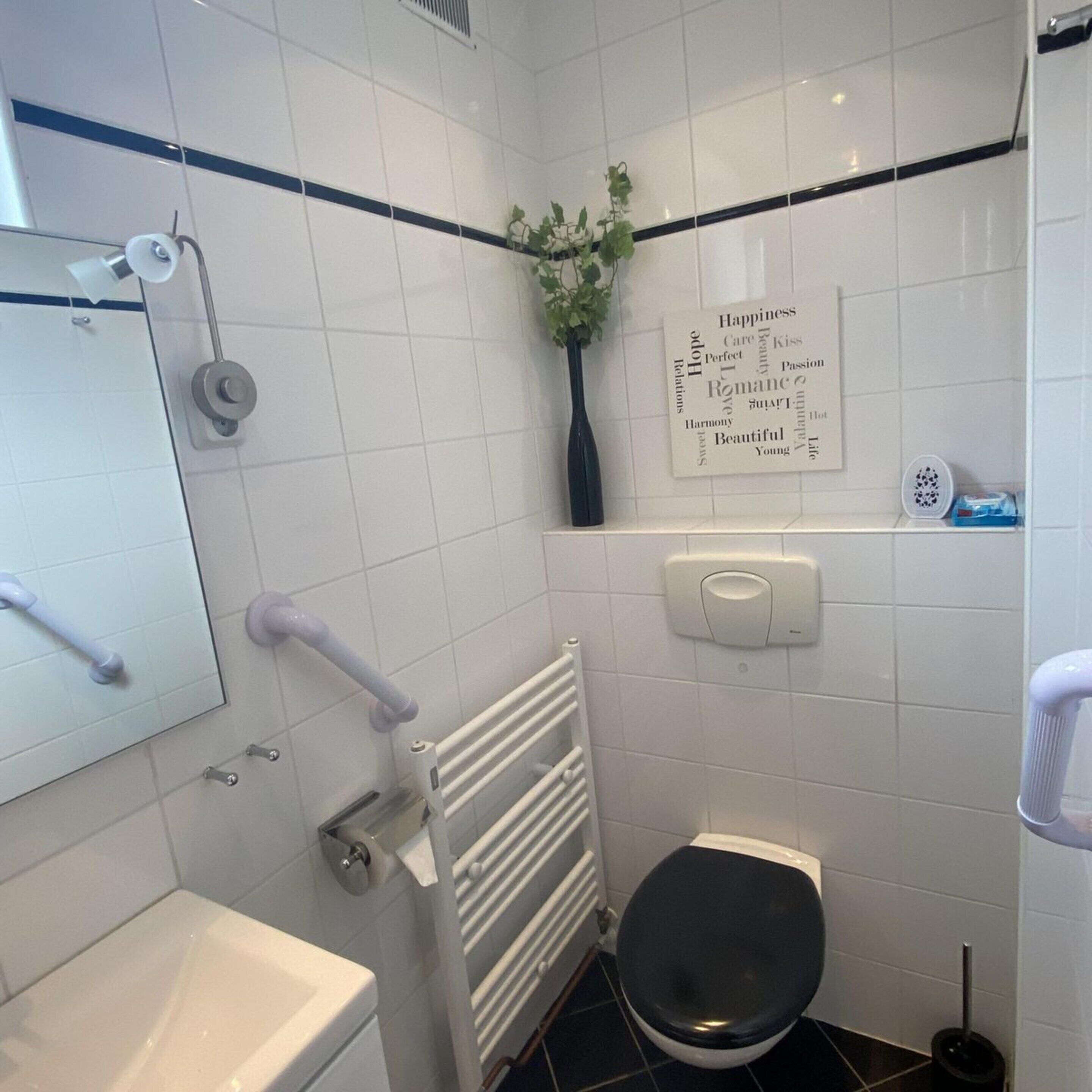 Une petite salle de bain moderne avec des carreaux blancs, des toilettes, un sèche-mains, un radiateur et un nuage de mots sur le mur.