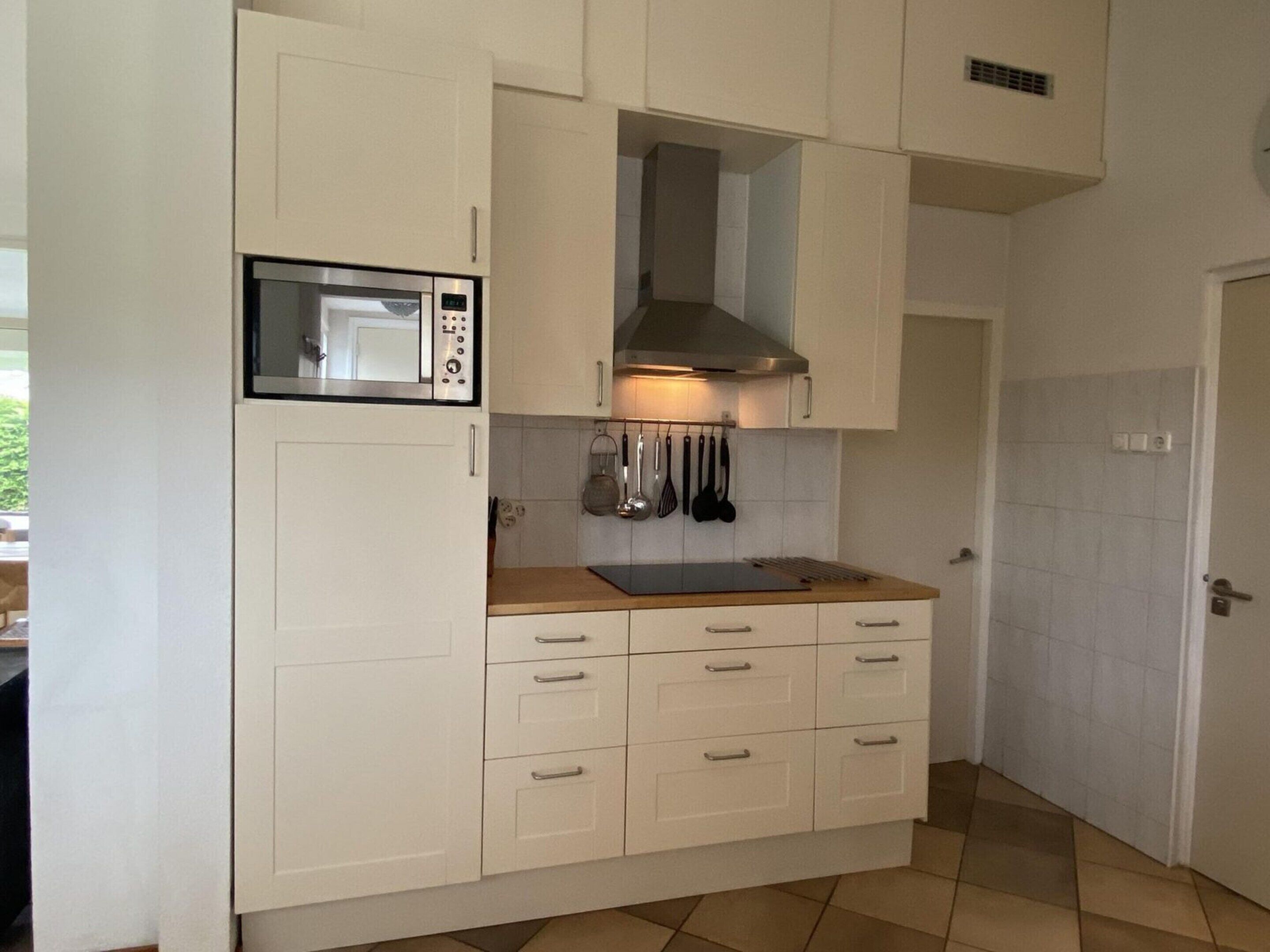 A compact kitchen with white cabinets, a microwave, a stove, and hanging utensils.