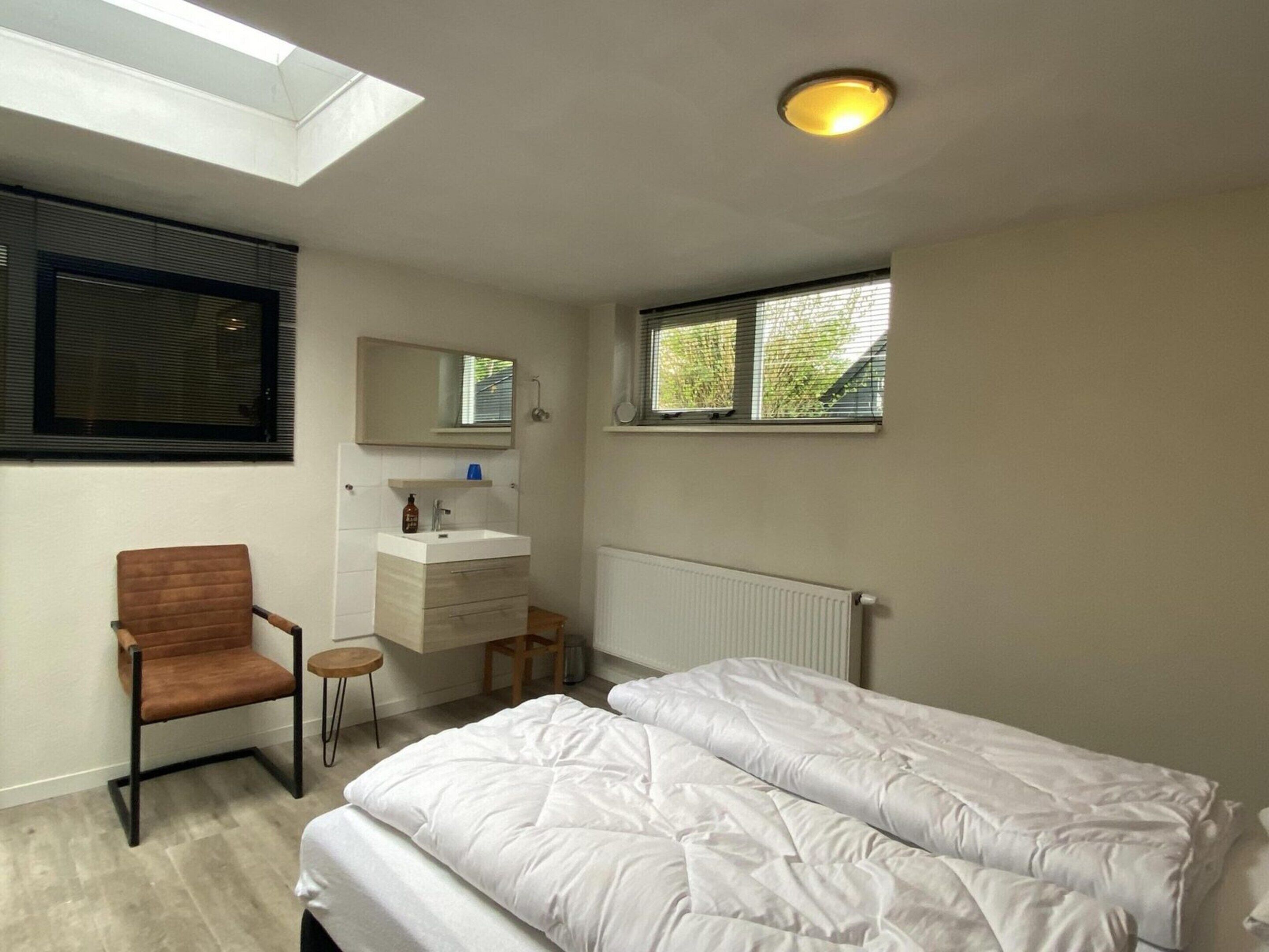 A bedroom with a skylight, a bed, a chair, a bedside table, a mirror, a window, and a radiator.