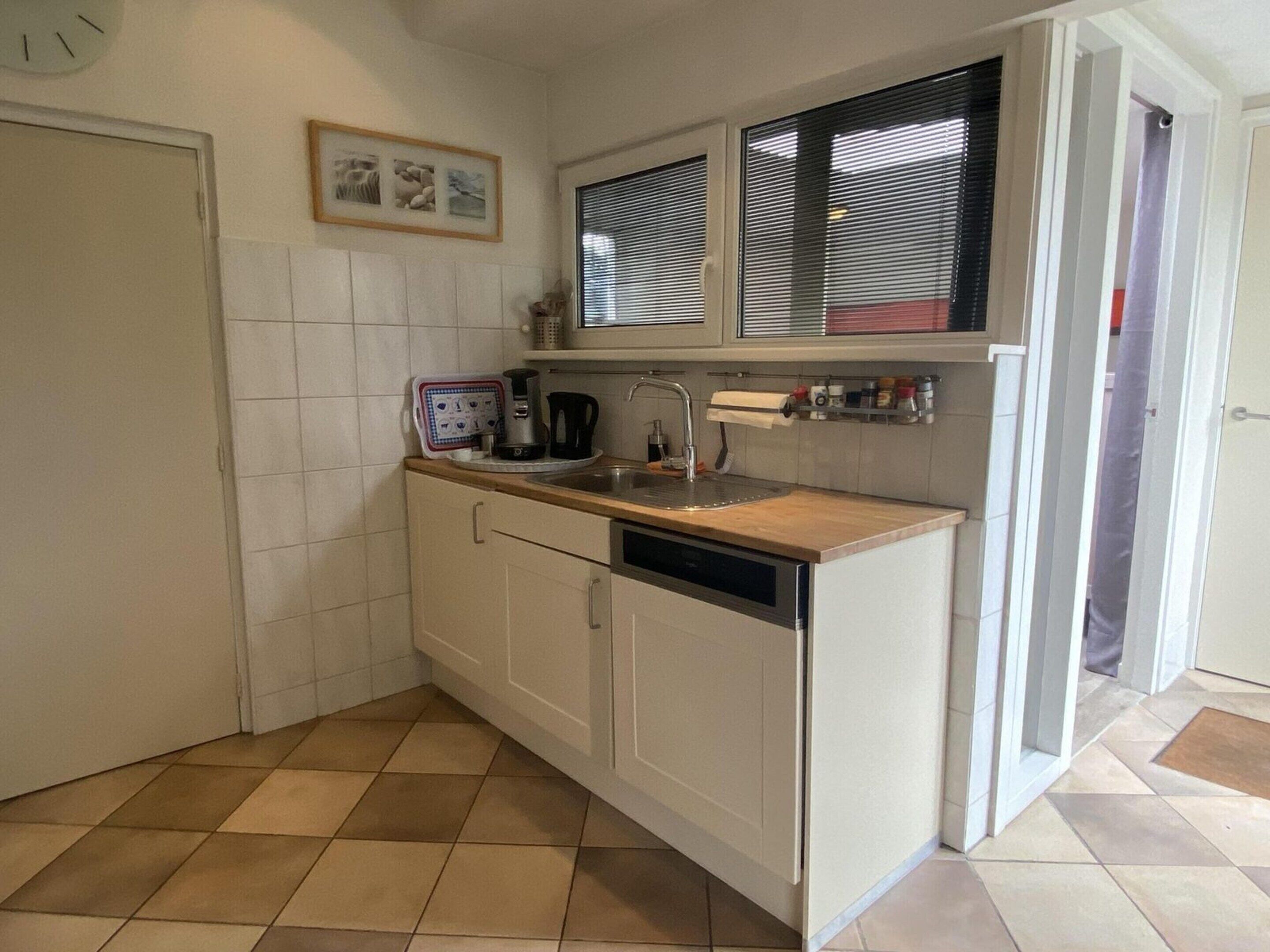 A compact kitchen with white cabinetry, a built-in dishwasher, a coffee maker, and a window with blinds.
