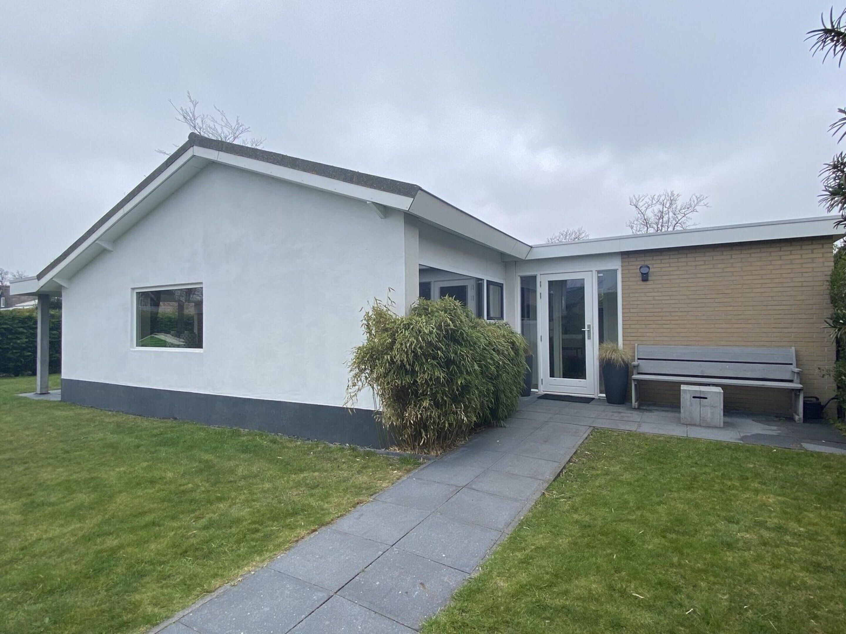 A modern two-story house with a white exterior, a small front yard, and a bench.