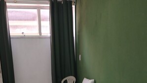 A hotel room with two beds, each with white linens and pillows. There is a window with curtains, a green wall, and a white chair. - Pousada Belo Mar (Salvador)
