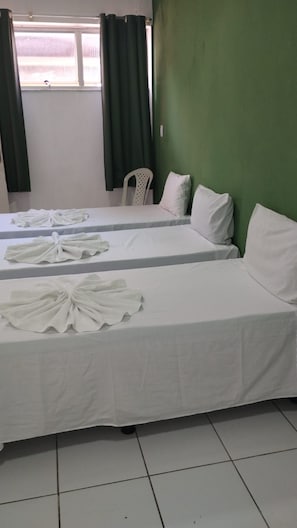 A hotel room with two beds, each with white linens and pillows. There is a window with curtains, a green wall, and a white chair. - Pousada Belo Mar (Salvador)