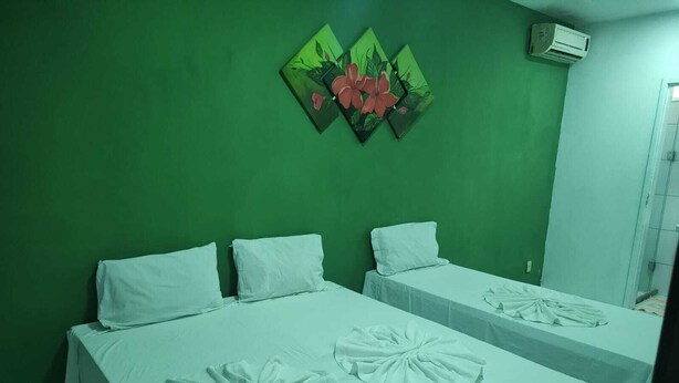 Une chambre avec deux lits, chacun étant équipé de draps blancs et d’une serviette posée sur le lit. Un mur est peint en vert et un tableau représentant des fleurs est accroché au-dessus des lits.