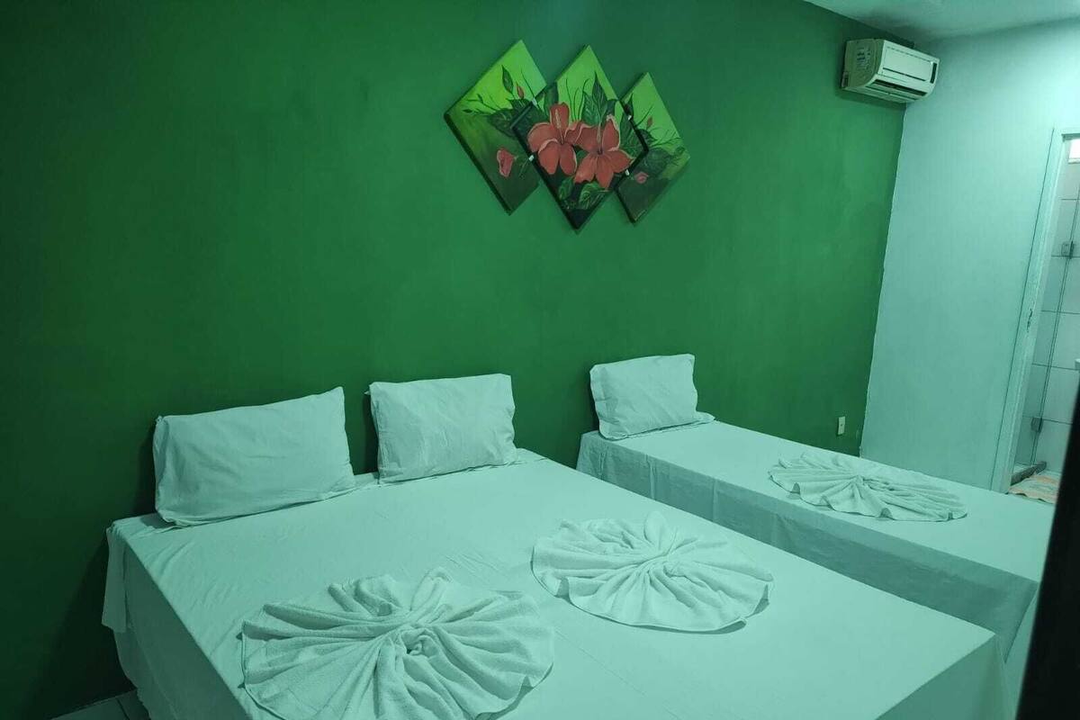 Ein Zimmer mit zwei Betten, jeweils mit weißer Bettwäsche und einem Handtuch auf dem Bett. Eine grüne Wand und ein Blumenbild hängt über den Betten.