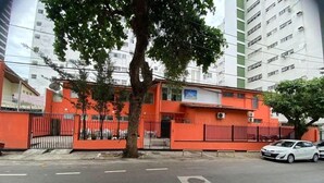 Un bâtiment à la façade rouge, doté d’une entrée fermée par un portail et d’un arbre devant.