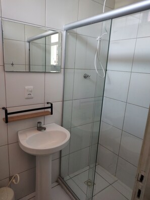 Un baño con lavamanos blanco, espejo y cabina de ducha de vidrio.