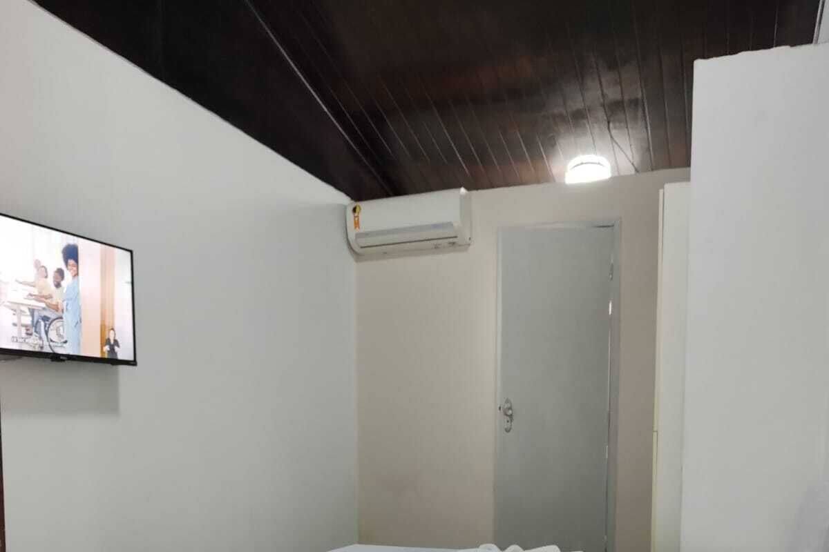 Ein Zimmer mit einem Einzelbett, Fliesenboden, weißer Bettdecke, einem an der Wand montierten Flachbildfernseher und einer Tür mit Spiegel.